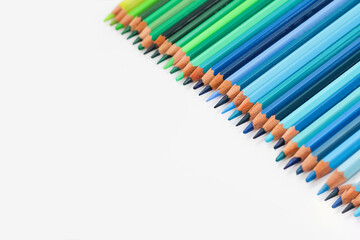 Multi-colored pencils lie on a white table, the blue range of colors