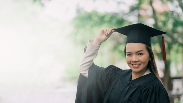 Study, education, university, college, graduate concept. Adult female Asian student in academic gown and graduation hat standing outside college.