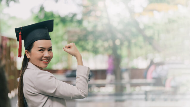 Study, education, university, college, graduate concept. Adult female Asian student in academic gown and graduation hat standing outside college.