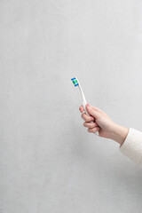 Morning concept, toothbrush in the hands of a young woman on a gray background.