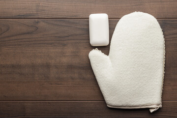 Bath glove with soap bar on the table. Shower glove and bar of soap on wooden background. Flat lay...