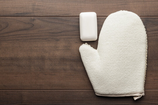 Bath Glove With Soap Bar On The Table. Shower Glove And Bar Of Soap On Wooden Background. Flat Lay Photo Of Bath Glove With Copy Space.