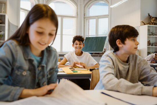 Portrait of happy schoolboy sitting at desk with friends in classroom