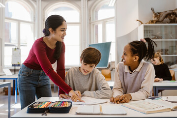 Happy teacher looking at female student while assisting in classroom