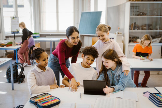 Teacher with male and female students using tablet PC at desk in classroom