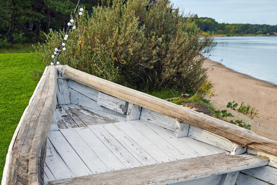 The nose of a wooden old boat painted with white paint on a green meadow on the lake