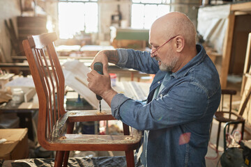 Fototapeta na wymiar Side view portrait of senior man repairing old furniture in carpentry workshop, copy space