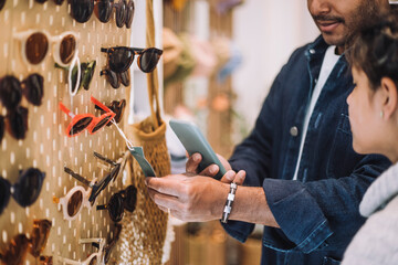 Man photographing label on sunglasses at rack by daughter in fashion store