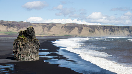 Large stone on a black sand beach with waves on the beach