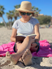 baby boomer woman with good purchasing power relaxing on vacation at the beach enjoying reading a book in the sunshine