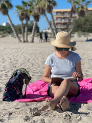 baby boomer woman with good purchasing power relaxing on vacation at the beach enjoying reading a book in the sunshine