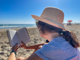 baby boomer woman with good purchasing power relaxing on vacation at the beach enjoying reading a book in the sunshine