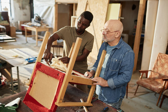 Portrait of senior craftsman with apprentice repairing old furniture in carpentry workshop
