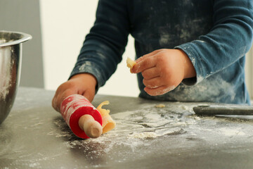 Cute toddler boy baking Christmas cookies at home. Red rolling pin and cookie cutters on dark grey...