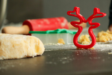 Red cookie cutter in shape of a deer with raw dough for Christmas cookies, blurred background with copy space