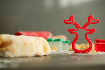 Red cookie cutter in shape of a deer with raw dough for Christmas cookies, blurred background with...
