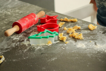 Preparation of raw dough for Christmas cookies, with red cutters and rolling pin on grey table at home.