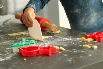 Close up of little boys hands making Christmas cookies at home. Red rolling pin and cookie cutters on grey kitchen table.