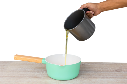 Pour the vegetable oil into the green pan on wooden table for cooking isolated on white background.PNG