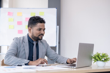 Young handsome happy man working in office on laptop and smiling