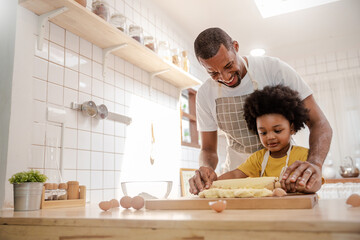 Portrait of African American dad little son having fun in kitchen home, baking pastry in modern...