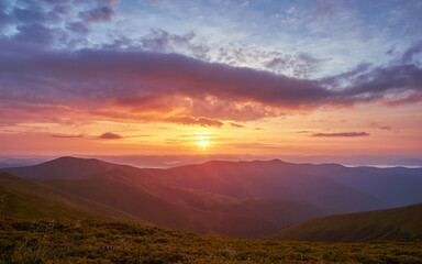 Picturesque sunrise in summer Carpathian mountains. Sun among dramatic clouds