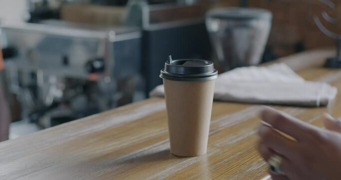 Close-up slow motion of barista giving to go coffee cup to customer in modern cafeteria. Take away drink and modern lifestyle concept.
