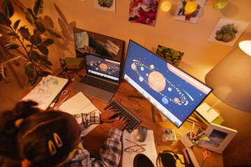 Top view at black girl using computer with space theme while studying at home in cozy evening light, copy space