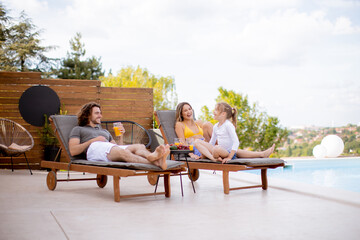 Young family relaxing by the swimming pool in the house backyard