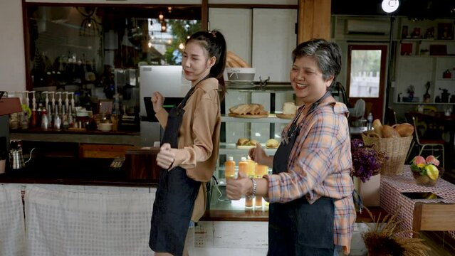 Retired Senior mother with Asian daughter, standing in front checkout orders inside cafe, which is its own bakery, mother daughter stood danced in front counter with emotion, good that sale is good.