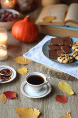 Cup of tea or coffee, plate with desserts, dried oranges, bowl of grapes, scented candles, vintage books, pumpkins and autumn leaves on the table. Autumnal hygge. Selective focus.