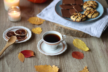 Cup of tea or coffee, plate with desserts, dried oranges, bowl of grapes, scented candles, vintage books, pumpkins and autumn leaves on the table. Autumnal hygge. Selective focus.