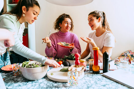 Woman serving lunch while female friends talking at home