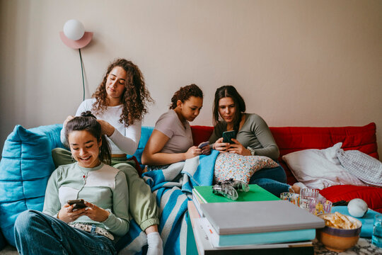 Happy female friends using smart phones in living room at home