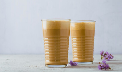 Two glasses of coffee latte with purple flowers on a light background, close up