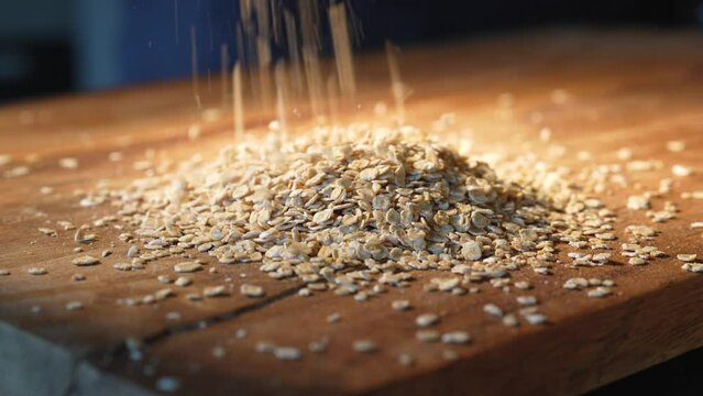 Fine oat flakes trop from above on a wooden table. Close-up.