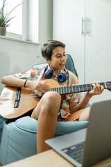 Smiling teenage girl making music with her guitar in the bedroom at home