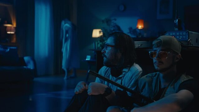 Two ghost hunters hiding behind the table. A female silhouette , ghost, entity standing on the background, then running towards them. The men are scared and frightened.