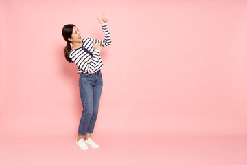 Young beautiful Asian woman smiling and pointing to empty copy space isolated on pink background,...