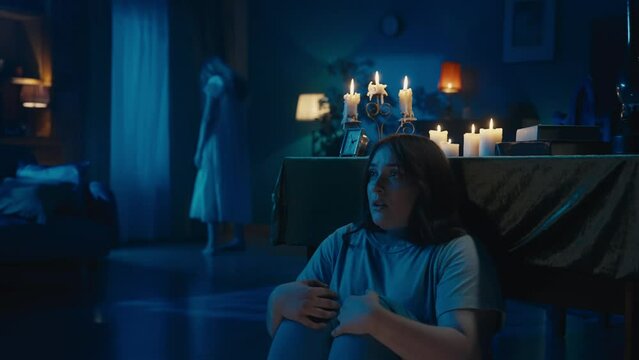 Video of a young woman sitting, hiding behind the table from from an otherwordly creature, entity, ghost. Woman calls somebody, looking back.