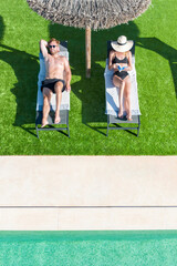 Couple relaxing on loungers under a parasol by the swimming pool - 0054