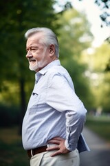 Naklejka na ściany i meble closeup shot of a senior man experiencing back pain while walking outdoors