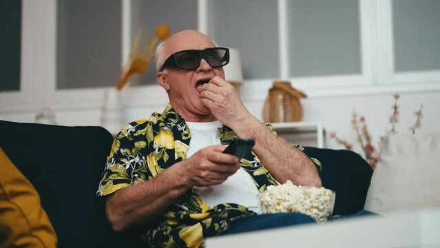 Funny senior man in 3D glasses watching movie and eating popcorn, leisure time