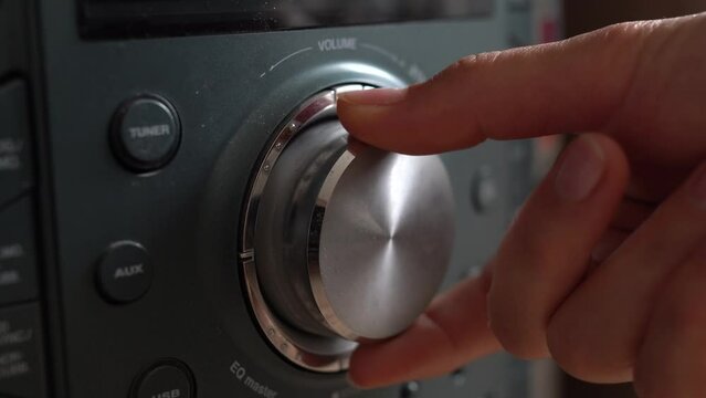 Close-up of a female hand turning on and increasing music volume knob on music center. View on control panel with tumblers, knobs and buttons on home theater amplifier. Video footage in 4K 25FPS