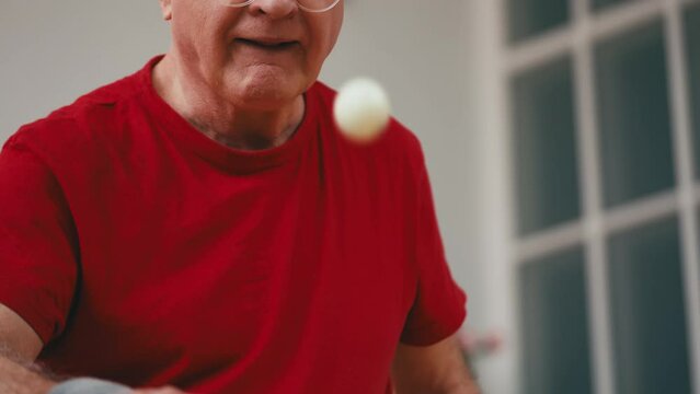 Senior man in sportswear bouncing table tennis ball on a racket at home, hobby
