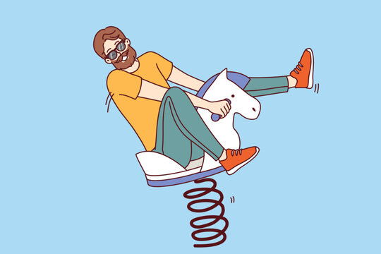Playful man sits on wooden rocking horse and enjoys children games, behaves like child of adolescence. Bearded man in sunglasses looks at screen, is childish and does not want to grow up