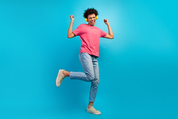 Full size photo of attractive young man raise fists earphones dancing dressed stylish pink clothes isolated on blue color background