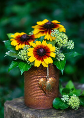 Flower arrangement with yellow and orange globular or Black Eyed Susan flowers and ivy blossom in rusty tins with rustic heart in the summer garden. Gardening concept. Selective focus.
