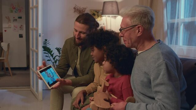 Medium Shot Of Male Members Of Family With Father, Sons And Grandfather Talking On Video Call With Friends On Digital Tablet While Sitting On Sofa