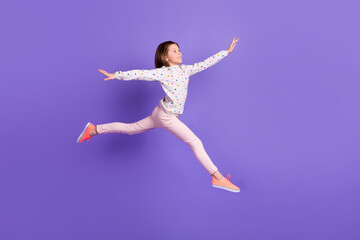 Full length photo of excited carefree little girl dressed dotted pullover running jumping high isolated purple color background